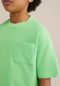 Zaļa, teksturēta īsā piedurkne T-krekls ar kabatu kreisajā krūtīs. Ribota apkakle un birka labajā piedurknē.