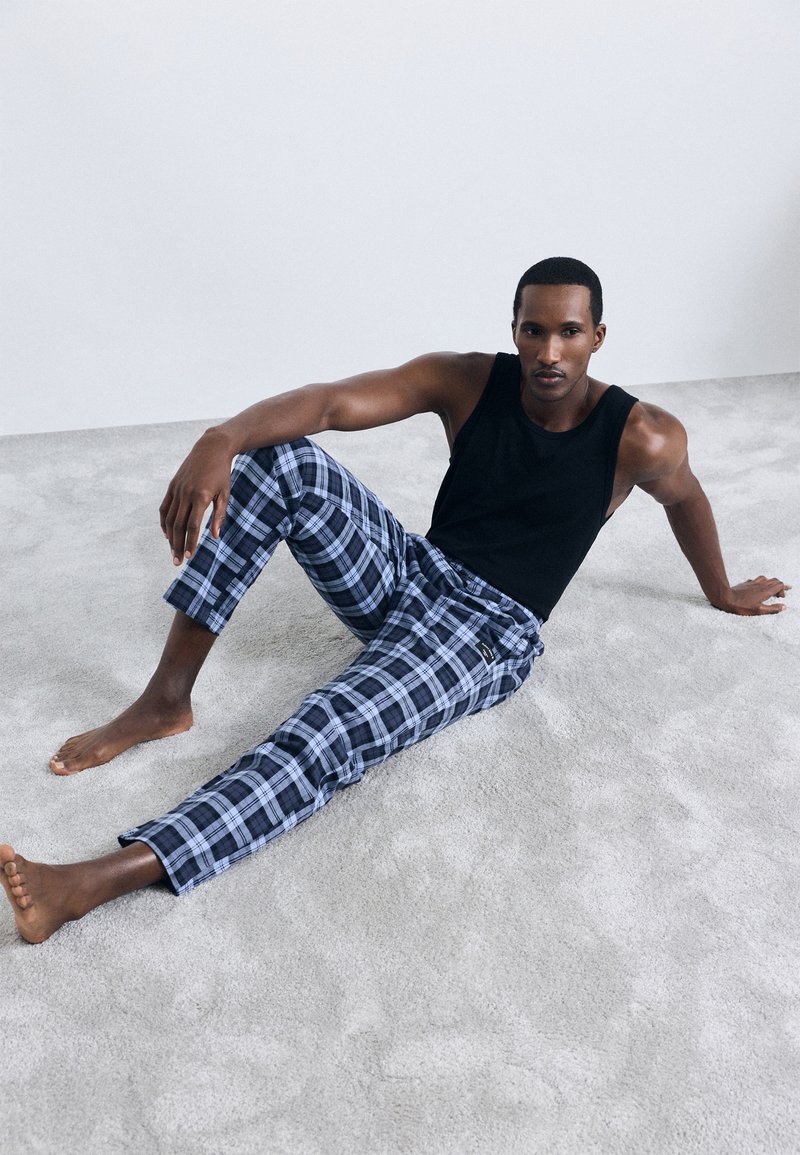 Crna majica bez rukava i plave karirane hlače za opuštanje s manžetama. Tkanina je lagana, s glatkom teksturom i suptilnim detaljima uzorka.