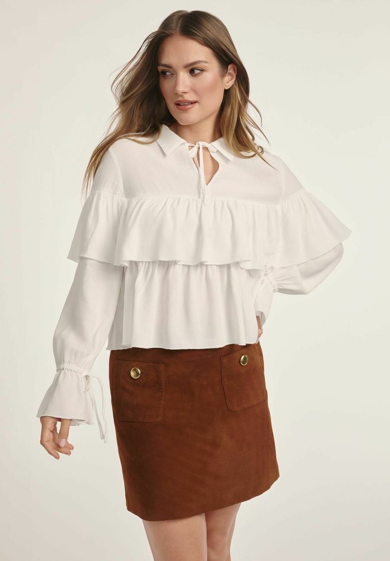 Biała bluzka z falbaniastymi warstwami i wiązanym dekoltem, zestawiona z brązową zamszową spódnicą z złotymi guzikami i dwiema przednimi kieszeniami.