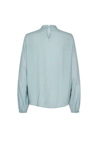 Ljusblå blus med ett litet rutmönster, långa ärmar, rynkade manschetter och en nyckelhålsöppning bak i nacken. Mjuk tyg.