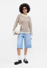 Beige ja kreemivärvi triibuline sviiter, helesinised denimpüksid, mustad platvormkingad ja valged pahkluu sokid. Hoides valget kotti.