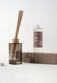 Mørk glas aromadiffuser med trælåg og fem bambuspinde, ved siden af en gennemsigtig duftrefill-flaske på en mønstret papæske.