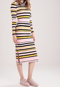 Abito a righe con maniche lunghe, scollo a giro e spacchi laterali. I colori includono rosa, nero, giallo e bianco. Realizzato in tessuto a costine.