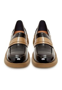 Paire de mocassins en cuir verni noir avec larges brides beiges et semelles assorties beiges, présentée de face sur un fond blanc.