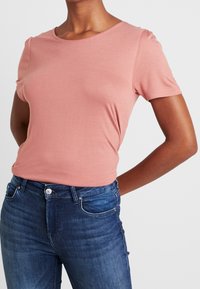 Lyserød kortærmet t-shirt med rund hals, afslappet pasform og blød tekstur, parret med mørkeblå jeans.