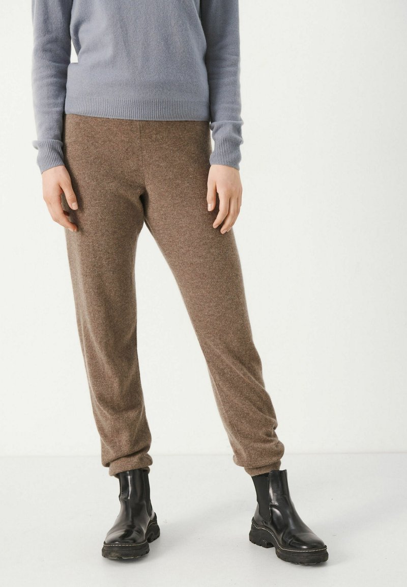 Joggers marrones de mezcla de lana con un ajuste tapered, que cuentan con puños acanalados. Combinados con un suéter azul claro y botas negras hasta el tobillo.
