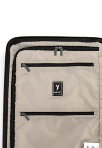 Interno di una borsa da viaggio in tessuto grigio che presenta numerosi scomparti neri con zip e un'etichetta logo nera. Tessuto morbido e materiali resistenti.