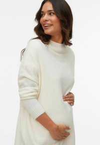 Pull en tricot de couleur crème avec un col roulé côtelé et des manches retroussées. Présente une coupe décontractée et une texture douce, idéale pour le superposition.