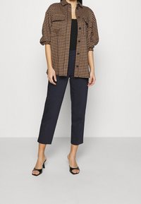 Brun och svart rutigt mönstrad skjorta, knäppt, med två bröstfickor, tillsammans med marinblå korta byxor och svarta slip-on klackar.