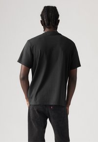 Tricou din bumbac negru, cu mânecă scurtă, cu un croi lejer, având guler rotund. Purtat cu blugi negri. Design minimalist, fără modele sau grafice vizibile.