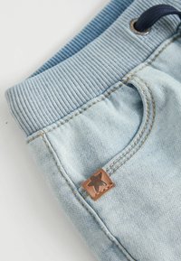 Shorts en coton bleu clair avec une taille côtelée et un patch en étoile marron, présentant des coutures tonales et une poche latérale.