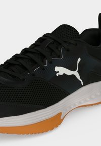 Μαύρο αθλητικό παπούτσι Puma με λευκή σόλα, πορτοκαλί πέλμα, μαύρα κορδόνια, επάνω μέρος από δίχτυ και λευκό λογότυπο Puma στο πλάι.