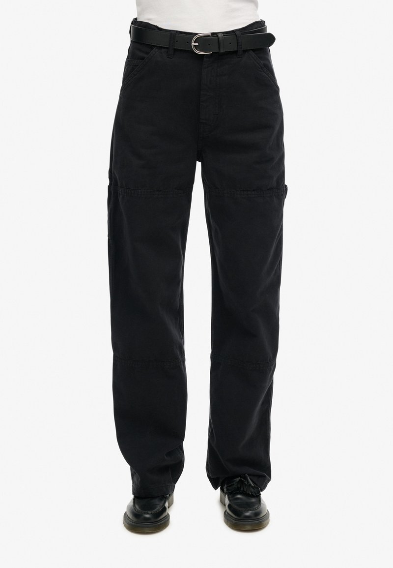 Schwarze Cargo-Hosen aus Baumwolle, mit lässiger Passform, mehreren Taschen und genähten Nahtdetails. Getragen mit einem schwarzen Gürtel und Schuhen.