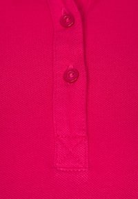 Fuchsia polo skjorta med tre knappar vid halsringningen, med ett texturerat tyg och broderade detaljer på kragen och fållen.