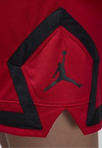 Punaiset koripalloshortsit, joissa on teksturoitu kangas. Niissä on musta kolmionmuotoinen korostus ja musta Jumpman-logo helman lähellä.