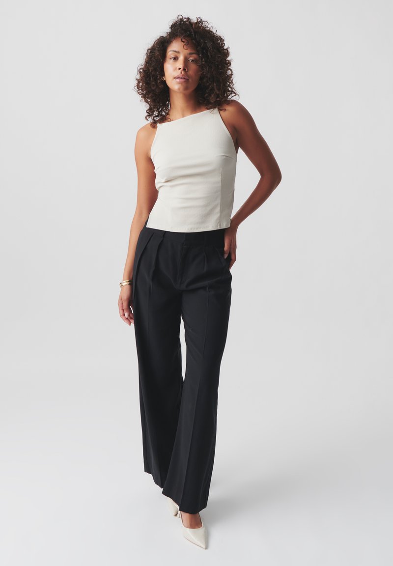 Light beige sleeveless top with square neckline, paired with high-waisted black wide-leg trousers and pointed white heels. Smooth texture.