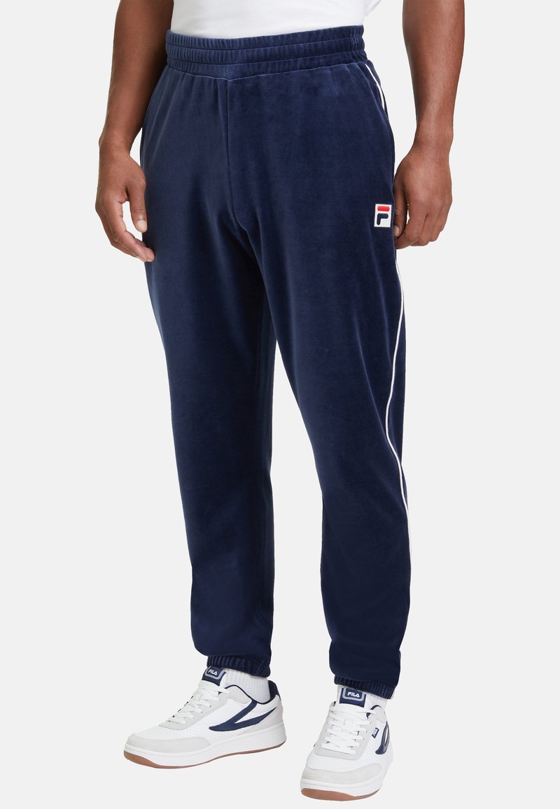 Marinblå velourbyxor med elastisk midja och muddar, med vita sidostripes och en rödvit logotyp på höften.