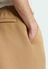 Light beige joggers with a soft texture, featuring a side pocket and a waistband with an elastic finish for comfortable fit.