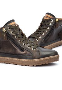 Zapatillas altas de cuero marrón con detalles en verde oliva, que cuentan con herrajes de latón, cremalleras doradas y suelas de goma texturizada para mayor agarre.