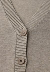 Cardigan beige con scollo a V, texture a costine e due bottoni circolari di colore marrone chiaro. Tessuto morbido con una finitura liscia.