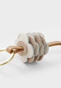 Leather keychain featuring layered flower shapes in beige, cream, and light blue, attached to a gold metal ring with a tan leather strap.