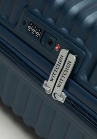 Valigia rigida blu navy con texture a righe verticali, cerniere argentate, lucchetto a combinazione e nome del marchio "Wittchen" sui tiranti delle cerniere.