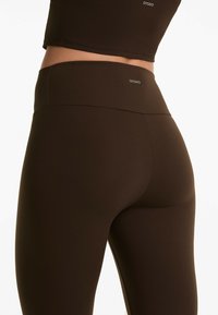 Brown leggings with a high waistband and smooth texture. Branding "OYSHO" is visible on the waistband. The design is form-fitting.