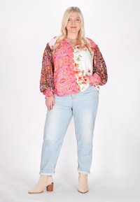 Blusa multicolore con motivi paisley rosa e floreali, caratterizzata da maniche voluminose a fantasia; abbinata a jeans azzurri chiari e stivali alla caviglia beige.