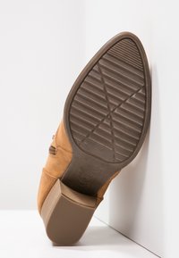 Botas de ante color tostado con punta redonda y suela de goma texturizada. Incluyen un zipper lateral y un tacón bajo apilado.