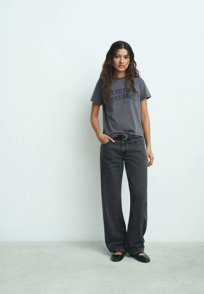 T-shirt graphique gris avec le texte "Rêves Électriques", associé à un pantalon large noir taille haute et des ballerines noires. Design simple et décontracté.