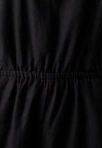 Tela negra con detalle de cintura elástica fruncida, que muestra una textura suave y un acabado liso. El diseño presenta arrugas sutiles y drapeados.