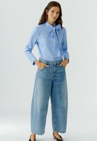 Lichtblauw gestreepte blouse met een strikje bij de kraag, gecombineerd met wijdvallende vervaagde denimjeans en zwarte platte schoenen.