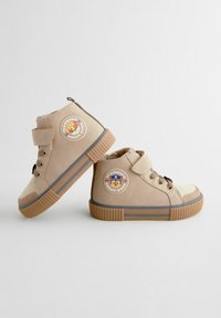Scarpe alte marroni con accenti in mesh testurizzato, suole in gomma, cinturini regolabili in velcro e un logo circolare che presenta un personaggio.