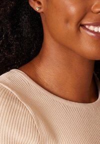 Boucles d'oreilles en or en forme de papillon, vue en gros plan. Encolure d'un pull côtelé beige doux, texture de peau lisse, teinte naturelle, subtils creux.
