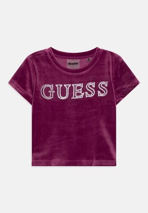 Fioletowa aksamitna koszula z krótkim rękawem, krótkiego kroju, z logo "GUESS" wysadzanym kryształkami na wysokości klatki piersiowej.