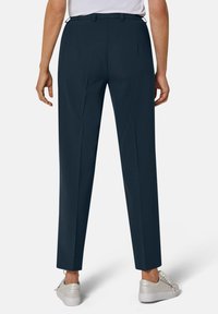 Marineblauwe broek met een rechte pasvorm, geplooid ontwerp en een hoge taille. Afgewerkt met riemlussen en gedragen met lichtgekleurde schoeisel.