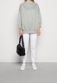 Grå sweatshirt med hög halsringning och Nike-logotyp, ihop med vita åtsittande sweatpants och vita sneakers. Håller en svart puffy handväska.