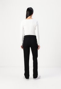 Μαύρο τζιν με tapered κόψιμο και πίσω τσέπες, συνδυασμένο με έν�α λευκό μακρυμάνικο μπλουζάκι με ραβδώσεις. Το μοντέλο φαίνεται από πίσω, φορώντας μαύρα αθλητικά. 