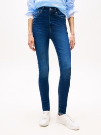 High-waisted skinny jeans in dark blue denim with a smooth texture and contrast stitching, paired with white sneakers.