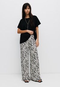 Zwarte oversized t-shirt gecombineerd met wijde broek met een zwart-wit zebra patroon; zachte stof, relaxte pasvorm, minimale accessoires.
