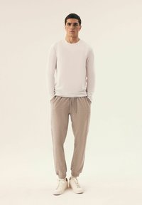 Weißes Langarmhemd, hellgraue Jogginghose und weiße Turnschuhe. Die Hose verfügt über einen elastischen Bund und Bündchen. Glatte, leichte Materialien.