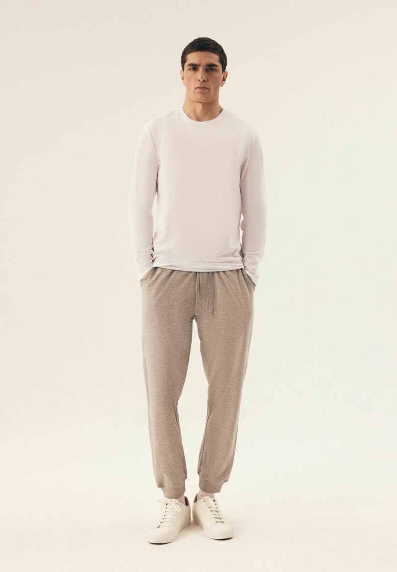 Weißes Langarmhemd, hellgraue Jogginghose und weiße Turnschuhe. Die Hose verfügt über einen elastischen Bund und Bündchen. Glatte, leichte Materialien.