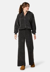 Dunkelgraues Cord-Loungewear-Set bestehend aus einem Reißverschluss-Hoodie mit Taschen und weit geschnittenen Hosen. Weiche Textur und lockerer Schnitt für hohen Komfort.