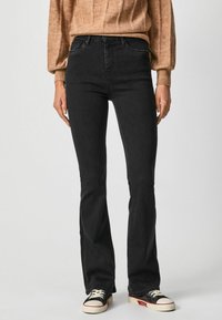 Jeans de corte acampanado en negro con una cintura alta, que presentan una textura de denim suave y detalles de costura mínimos, combinados con zapatillas en blanco y negro.