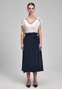 Falda midi de color azul marino con textura suave y cintas en la cintura, combinada con una blusa de manga corta blanca que presenta un ribete en contraste a lo largo del escote.