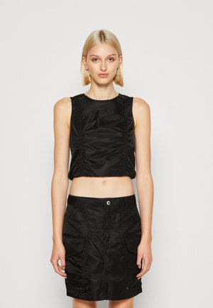 Schwarzes Crop-Top mit Raffungen, kombiniert mit einem schwarzen Rock mit Taschen, beide aus einem glatten, glänzenden Textil. Einfache, klare Linien.