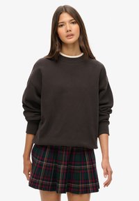Donkergrijze oversized sweatshirt met een ronde halslijn en omgeslagen lange mouwen, gecombineerd met een geplooide rok met een groen en rood ruitpatroon.