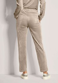 Beige veloursbroek met een zachte textuur en een elastische tailleband, met een recht model. Gemaakt met metallic-zilveren sneakers.