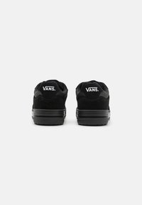Crne Vans tenisice s leđa, sa gornjim dijelom od antilopa, teksturiranom gumom i bijelim logom straga. Jednostavan, niskoprofilni dizajn.