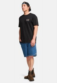 Zwart katoenen T-shirt met een klein kleurrijk graphic, gecombineerd met blauwe denim shorts en bruine enkellaarsjes met elastische zijkanten.